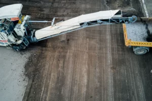 Operazione di fresatura dell'asfalto: una macchina specializzata rimuove e convoglia il fresato di asfalto su un camion per il trasporto
