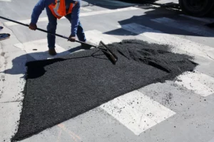 Operaio stende asfalto a freddo su una strada urbana durante lavori di manutenzione