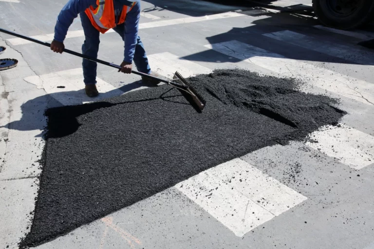 Operaio stende asfalto a freddo su una strada urbana durante lavori di manutenzione