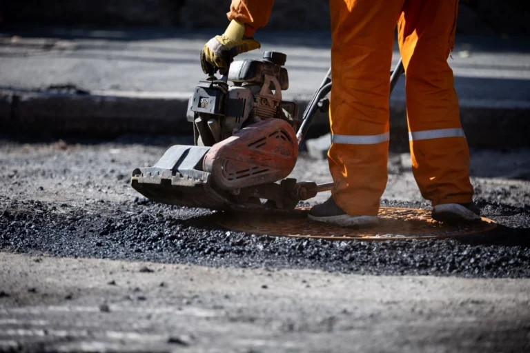 operaio procede con la manutenzione stradale, usa un compattatore per asfalto a freddo